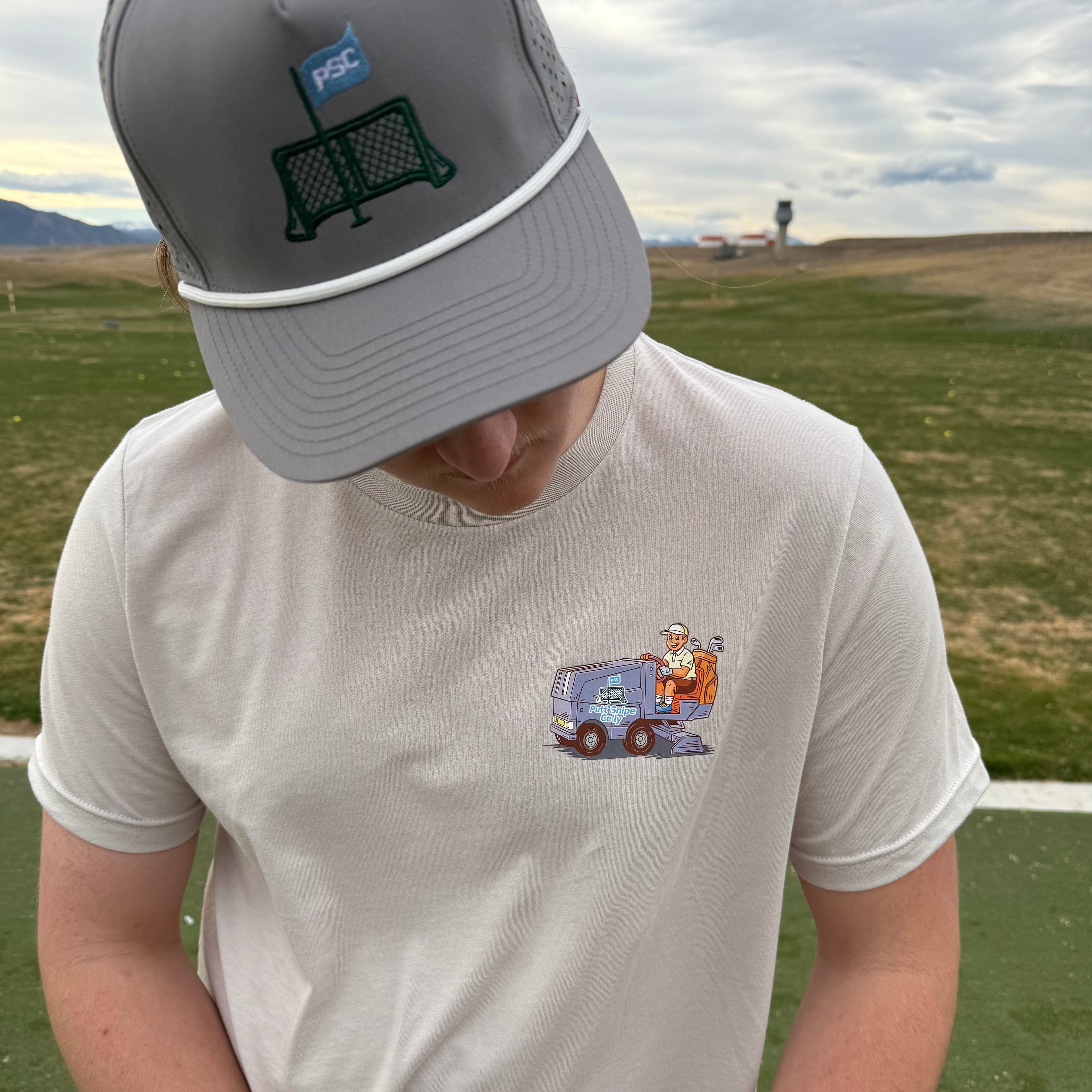 Close up view of the heather dust colored lifestyle t-shirt showing the unique Zam-Golf-Cart mashup from Putt Snipe Celly with the driving range in the background