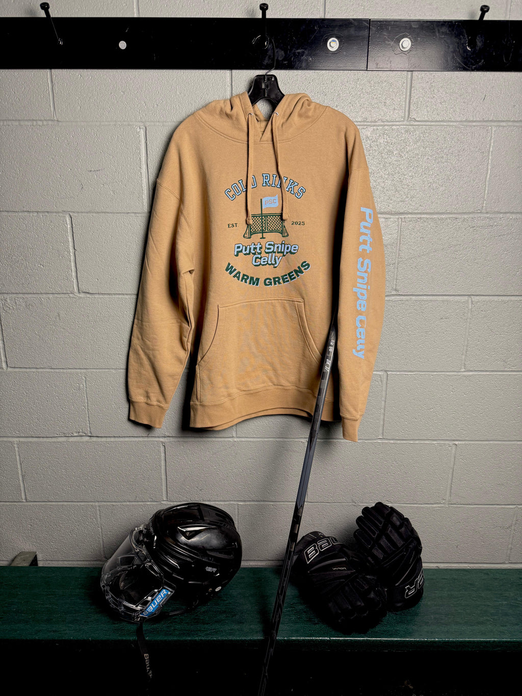 Locker Room setting featuring the Heritage design on the Sandstone colored hoodie showing both the main front design and signature word mark on left sleeve from Putt Snipe Celly.