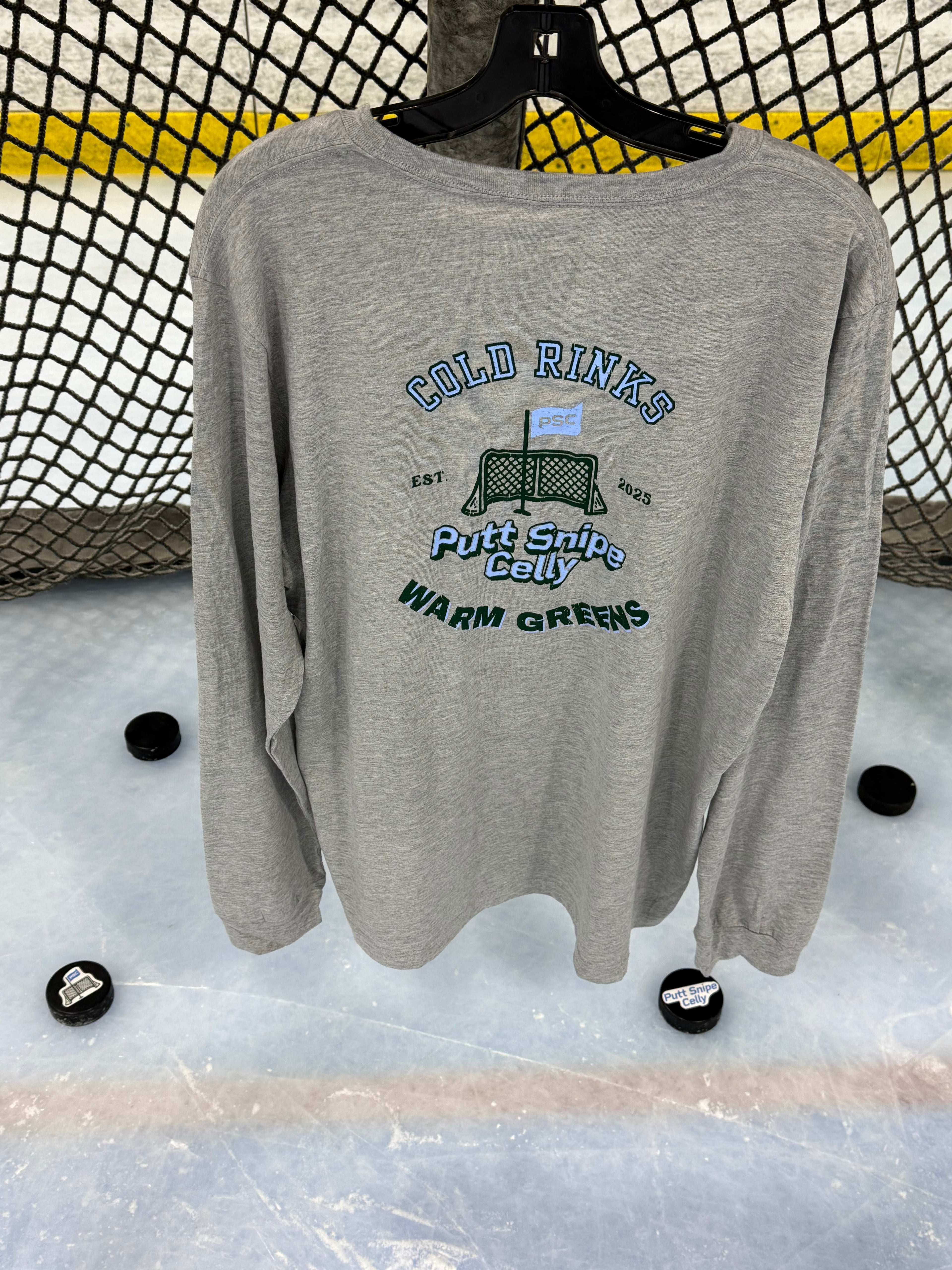 View of the back of the Heritage design in the athletic heather colored long sleeve lifestyle t-shirt shown hanging from a hockey net with pucks on the ice below. Presented by Putt Snipe Celly