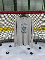 Heritage design in the athletic heather colored long sleeve lifestyle t-shirt shown hanging from a hockey net with pucks on the ice below. Presented by Putt Snipe Celly