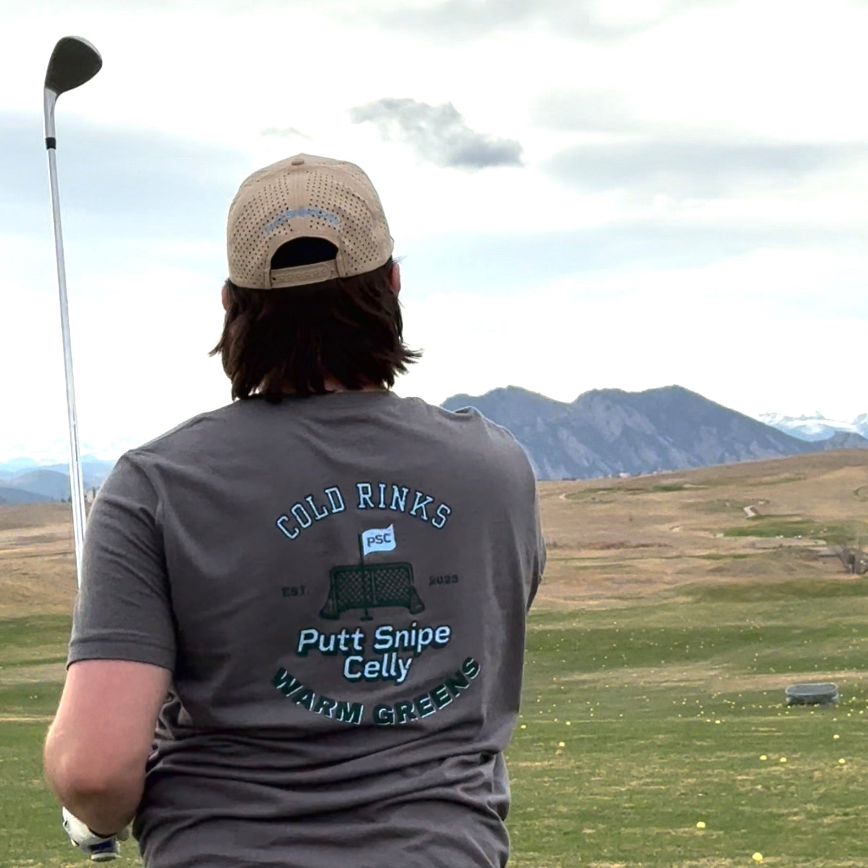 Co-founder Ryan as the driving range wearing the Heritage T-shirt featuring the full graphic Heritage design on the back of the shirt in the solid asphalt color. Proudly displaying the Putt Snipe Celly logo.