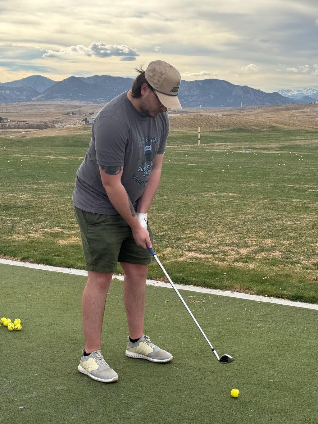 Co-founder Ryan at the driving range wearing the Heritage T-shirt featuring the full graphic Heritage design on the front of the shirt in the solid asphalt color. Proudly displaying the Putt Snipe Celly logo.