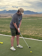 Co-founder Ryan at the driving range wearing the Heritage T-shirt featuring the full graphic Heritage design on the front of the shirt in the solid asphalt color. Proudly displaying the Putt Snipe Celly logo.